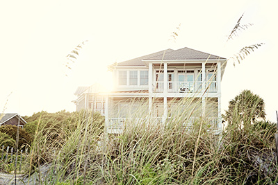 Ocean County home builders build beautiful homes like the one pictured which is taken at a distance and is backlit by bright sunlight and surrounded by beach grasses in the foreground