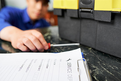 Toms River air conditioner repair man with tool in hand next to clipboard with an invoice attached. Also in frame is a black toolbox with a yellow top.